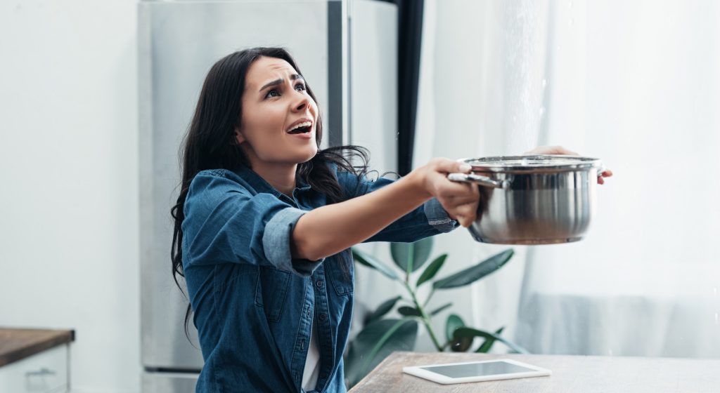 Worried woman in denim short with pot dealing with water damage in kitchen